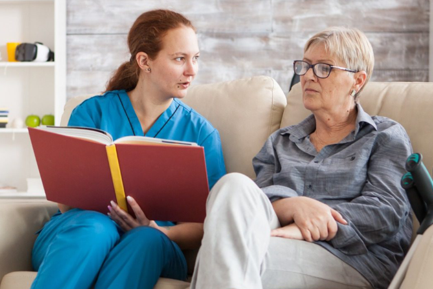 Caregiver Reading to Elderly Woman on Sofa, Providing In Home Care